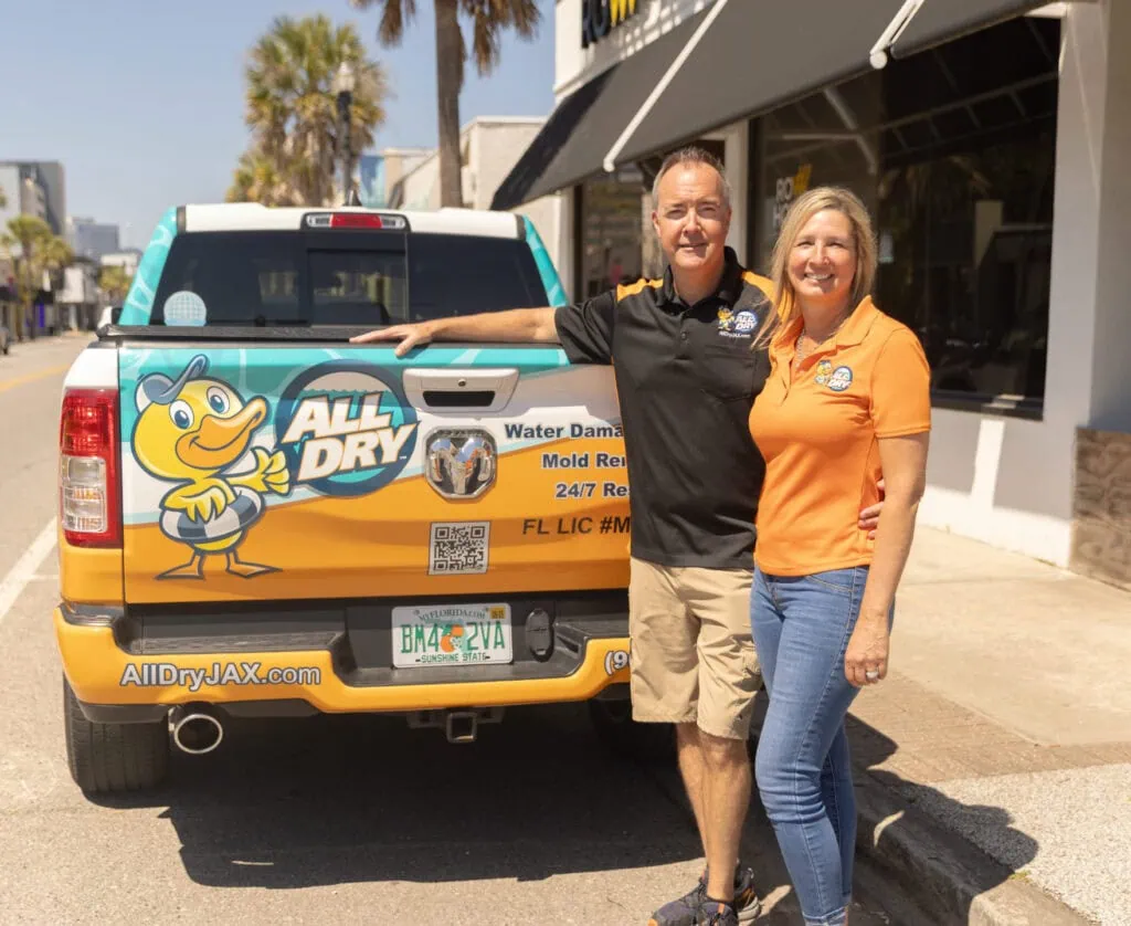 Todd and Harmony, owners of All Dry Services Jacksonville, in front of their service truck showing the logo and contact info.