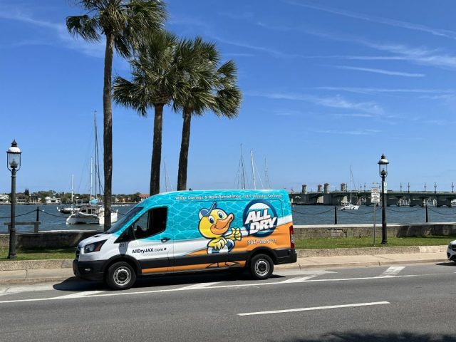 All Dry Services Jacksonville service van showing the logo and contact info parked on the side of the road in front of a bridge and St. Johns River